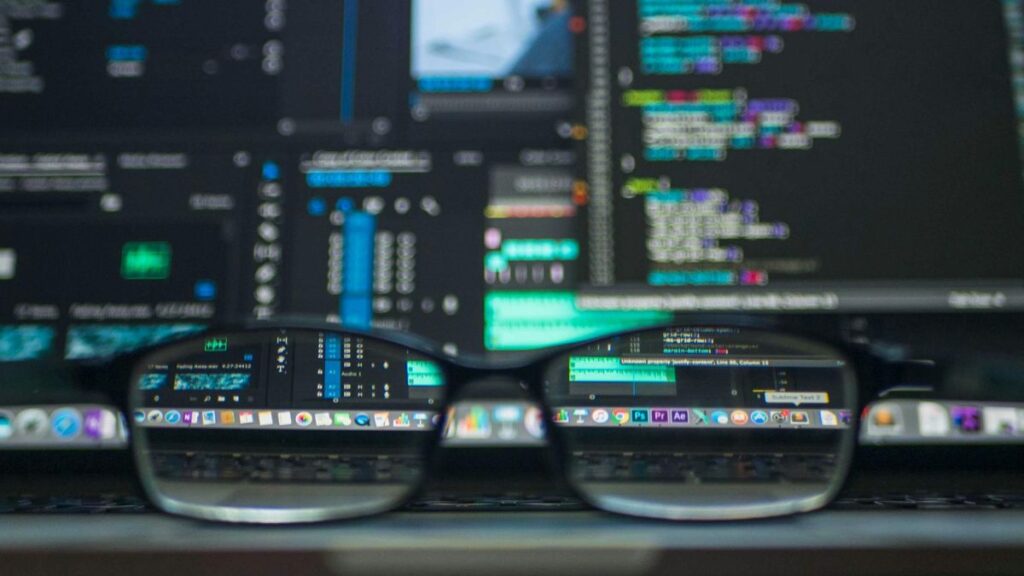 Close-up of computer screen with programming code and data analytics dashboard, viewed through eyeglasses, symbolizing data science and AI development.